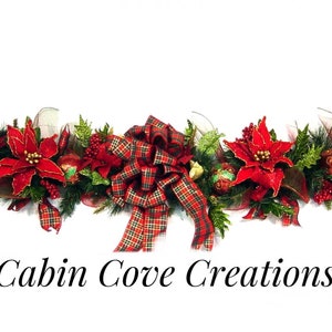 May include: A festive Christmas garland with red poinsettia flowers, green foliage, red and gold ornaments, and a plaid bow. The garland is perfect for decorating a mantel, doorway, or table for the holiday season.