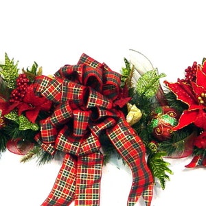 May include: A red and green Christmas garland with poinsettia flowers, red berries, and a plaid bow. The garland is decorated with gold glitter and is perfect for adding a festive touch to any home.