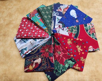 May include: A collection of folded Christmas-themed fabric squares arranged in a circular pattern. The fabrics feature various festive designs, including poinsettias, teddy bears, snowmen, and Santa Claus, in red, green, blue, and white colors.