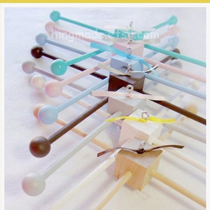May include: A wooden baby mobile with multiple colorful wooden dowels and wooden beads. The mobile is suspended from a wooden cube with a brown ribbon. The mobile is handmade in the USA.