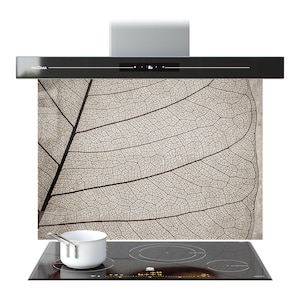 May include: A modern black range hood with a leaf design on the backsplash. The hood has a digital display and the brand name "PRISMA" is visible. A white saucepan sits on a black induction cooktop.