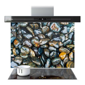 May include: A black range hood with a digital display above a glass panel showing a close-up of smooth, colourful river rocks. A white saucepan sits on a black induction hob.