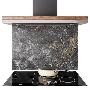 May include: A modern kitchen range hood with a black and wood finish, above a black hob. A marble backsplash with gold veining is behind the hob. A cream-coloured pot with a black lid sits on the hob.