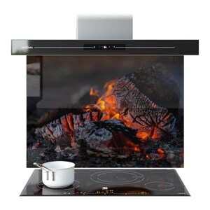 May include: A black range hood with the brand name "PRISMA" is mounted above a black glass cooktop. A white saucepan sits on the cooktop. The background features a glass panel with a fiery log image.