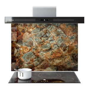 May include: A contemporary kitchen extractor fan with a black finish and a glass splashback displaying a rock texture in shades of brown, grey, and blue. A white saucepan sits on a black induction hob.