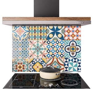 Può includere: Un paraschizzi da cucina con un motivo di piastrelle colorate con disegni geometrici e floreali in blu, giallo, rosso e verde. Un piano cottura nero con una pentola è di fronte al paraschizzi e una mensola di legno è sopra.