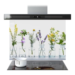 May include: A black range hood with the brand name "PRISMA" and a digital display. Below, a white panel features a floral arrangement in glass vases. A white saucepan sits on a black induction hob.