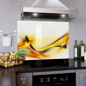 May include: A decorative kitchen backsplash with an abstract design in shades of yellow, orange, and gold. The backsplash is installed behind a black stovetop and beneath a stainless steel range hood. The kitchen features a black countertop and gray cabinets.