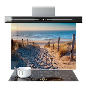 Puede incluir: Campana extractora negra con un panel de vidrio con una escena de playa. La campana tiene una pantalla digital y está montada sobre una placa de cocina negra con una olla blanca. La escena de la playa muestra un camino arenoso que conduce al mar.