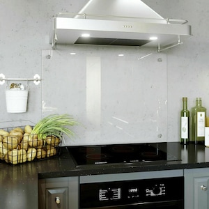 May include: A modern kitchen scene featuring a black stovetop, a stainless steel range hood, and a clear glass backsplash. A wire basket holds potatoes and green onions. Olive oil bottles are on the countertop.