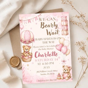 May include: A pink baby shower invitation with the text "We Can Bearly Wait" and "Charlotte". The invitation features a teddy bear in a hot air balloon, balloons, and a teddy bear holding a heart. The invitation is for a baby girl.
