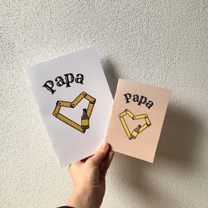 May include: Two cards with the word "Papa" in a script font. One card is white, the other is light brown. Each card features a yellow heart design made of a folding ruler and a beer bottle.