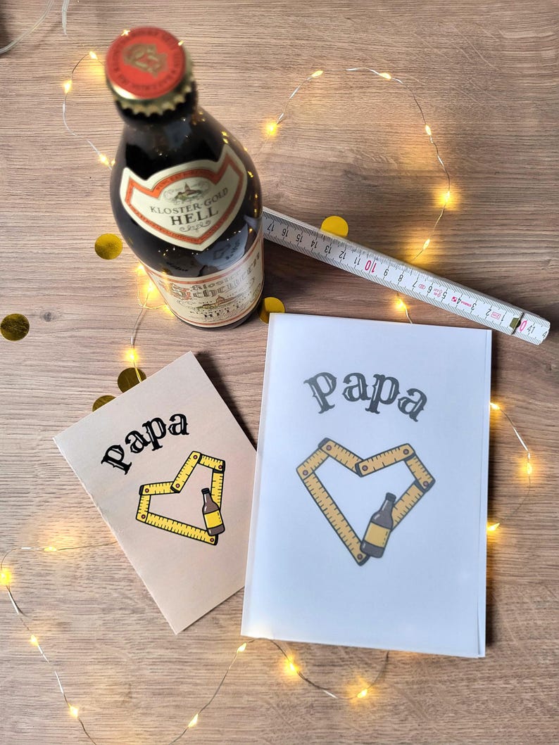 May include: Two greeting cards with the word "Papa" and a heart-shaped design made of a measuring tape and a beer bottle. A bottle of beer and a measuring tape are also present.