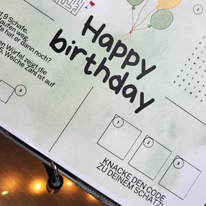 Könnte beinhalten: Ein bedrucktes Aktivitätsblatt mit dem Text Happy birthday, einem Labyrinth, einem Wortsuchrätsel und drei nummerierten Feldern. Das Blatt zeigt vier Luftballons in Grün, Orange und Gelb sowie den deutschen Text KNACKE DEN CODE ZU DEINEM SCHATZ!
