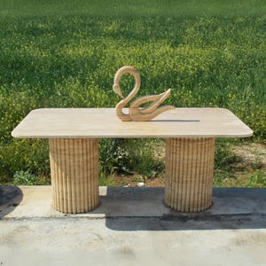 Puede incluir: Mesa rectangular beige con dos bases cil&iacute;ndricas. Una escultura de cisne de madera tallada se encuentra sobre la mesa. La mesa es de material claro, con un fondo de campo verde.