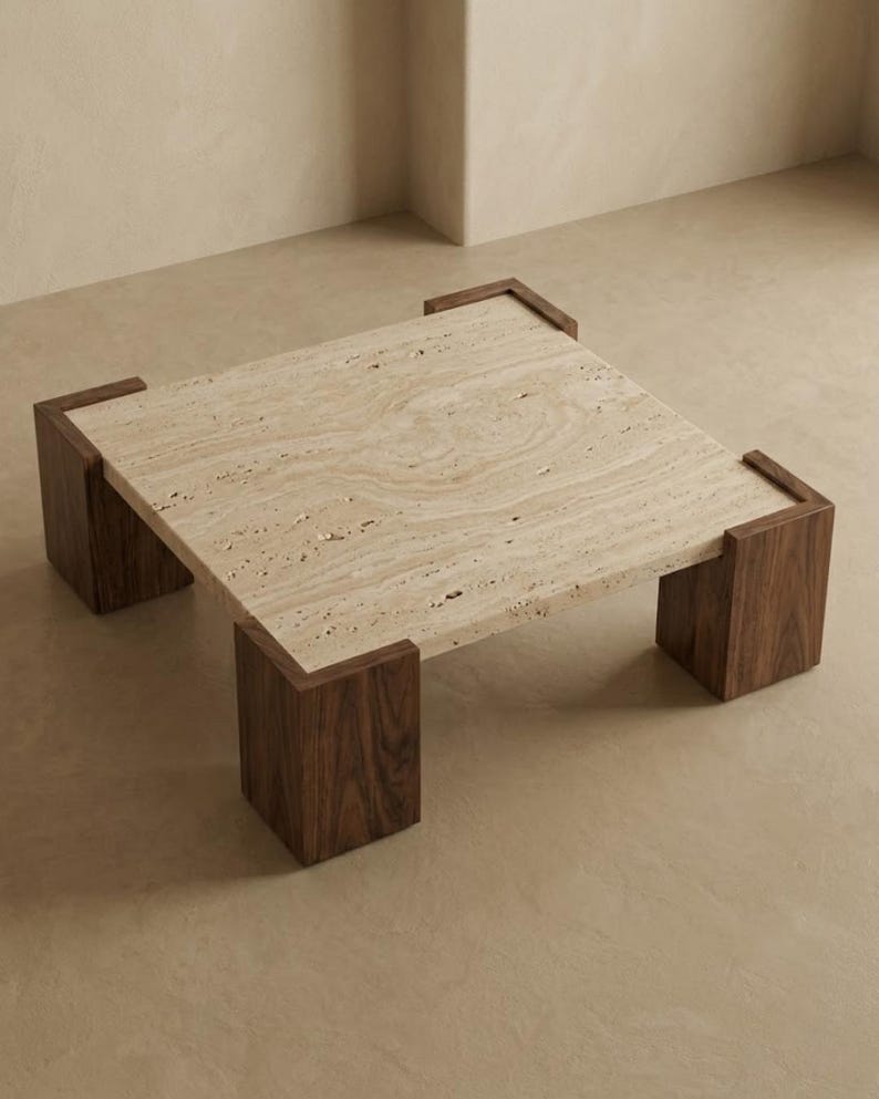 May include: A square coffee table featuring a beige, porous travertine stone top with natural veining. The table is supported by four thick, dark brown wooden legs that wrap around each corner of the stone surface, creating a sturdy frame.