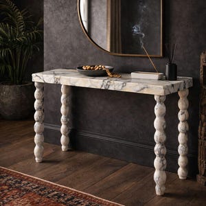 Puede incluir: Una consola con tapa de mármol y patas torneadas en forma de bolas apiladas. La mesa tiene un patrón veteado blanco y gris. Un espejo redondo con marco dorado cuelga sobre la mesa. Un cuenco decorativo y un quemador de incienso están sobre la mesa.