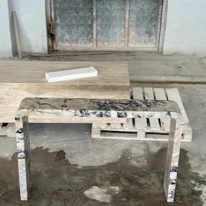 May include: A waterfall console table crafted from polished stone with a distinct white, beige, and black marbled pattern. The table features a continuous, smooth U-shaped design with rounded edges, showcasing natural veining throughout the surface.