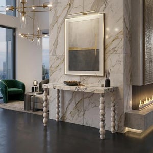 May include: A contemporary living room featuring a marble console table with turned legs, an abstract framed artwork, and a green armchair. The table holds a bowl and a black vase. A fireplace is also present.