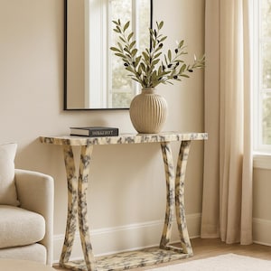 Può includere: Una consolle decorativa con piano effetto marmo e gambe curve. Un vaso con rami di ulivo è appoggiato sul tavolo, insieme a un libro. Uno specchio ad arco con cornice nera è appeso alla parete. La stanza ha una palette di colori neutri.