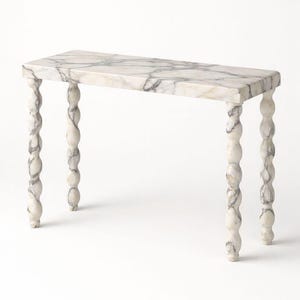May include: A rectangular marble console table with a white and grey veined pattern. The table has four ornate, twisted legs. The table is a decorative furniture piece.