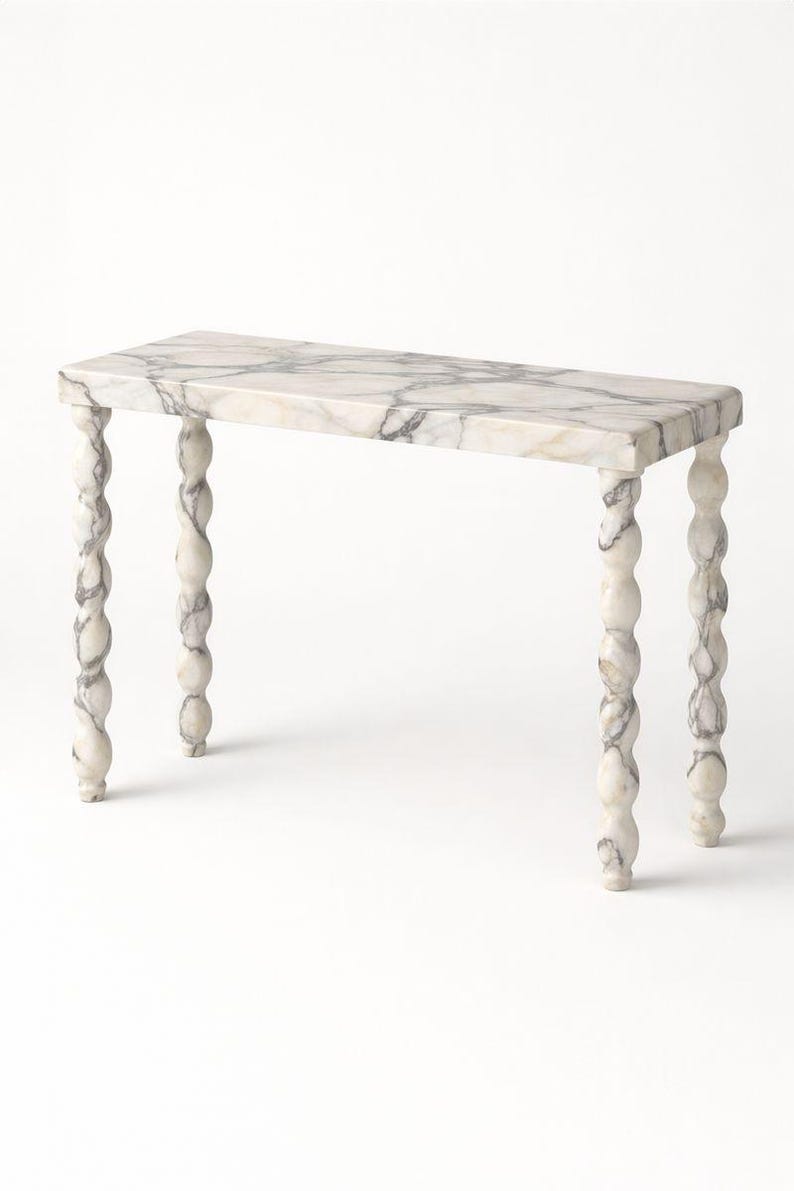 May include: A rectangular marble console table with a white and grey veined pattern. The table has four ornate, twisted legs. The table is a decorative furniture piece.