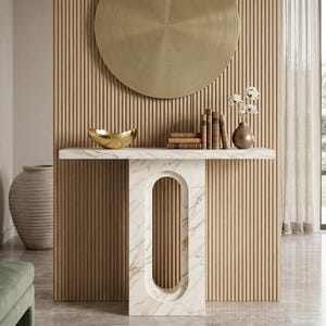 May include: A contemporary console table with a marble surface and an oval cut-out design. It features a gold bowl, books, and a vase with flowers. A large, circular, gold metal disc is mounted on the wood-panelled wall behind the table.