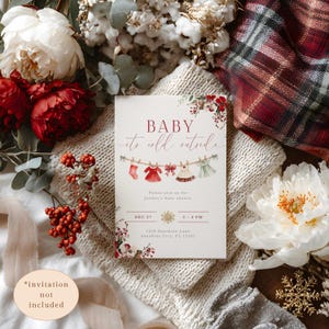 May include: A baby shower invitation with the text "BABY it's cold outside." The invitation features illustrations of baby clothes hanging on a clothesline. The design includes floral accents and the date and time of the shower.