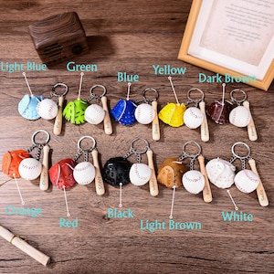 May include: A collection of ten baseball-themed keychains, each featuring a miniature glove in various colors, a white baseball, and a small wooden bat. The bats are engraved with names including Pat, Kelly, Daisy, Matthew, Kenny, Oliver, Steve, Wendy, Kyah, and Sadie.