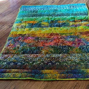 May include: A colorful, handmade quilt with horizontal stripes in shades of blue, green, yellow, orange, and purple. The quilt features various patterned fabrics and a green border. The quilt is approximately 30 inches wide and 40 inches long.