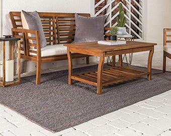 May include: Wooden outdoor furniture set comprising a bench, two chairs, and a coffee table. The set features grey cushions and a grey rug. A wooden lantern with a candle and a small side table with plants are also present.