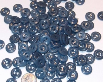 May include: A large pile of blue plastic buttons with two holes each. The buttons are all the same size and shape, and they are arranged in a random pattern.