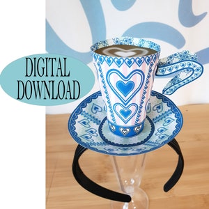 May include: A blue and white teacup and saucer headband with a heart pattern. The headband is black and the teacup has a pink and white striped pattern with blue hearts.