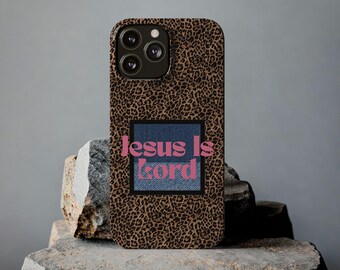Könnte beinhalten: Eine Handyhülle mit Leopardenmuster. Die Hülle hat einen Jeans-Patch mit dem pinkfarbenen Text "Jesus Is Lord". Die Handyhülle liegt auf einer Steinoberfläche.