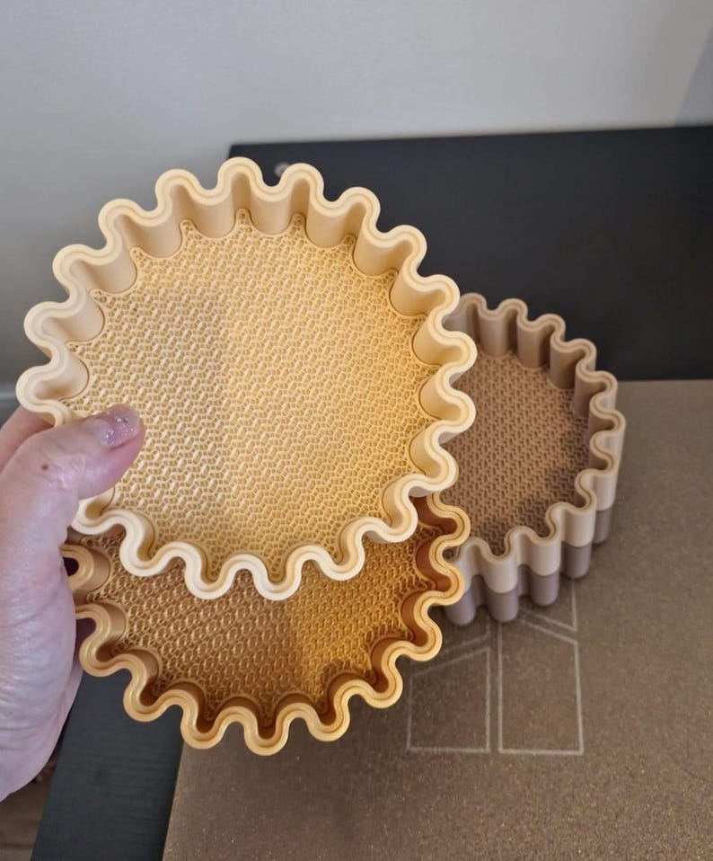 May include: Three beige, round, decorative trays with a wavy, scalloped edge. The trays have a textured interior surface. One tray is being held by a hand. The other two trays are stacked on top of each other.