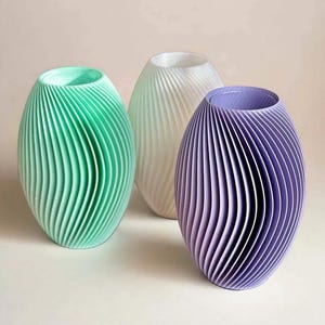 May include: Three decorative vases in shades of green, white, and purple. Each vase has a unique, ribbed design and an oval shape. The vases are arranged on a white surface, creating a modern and minimalist aesthetic.