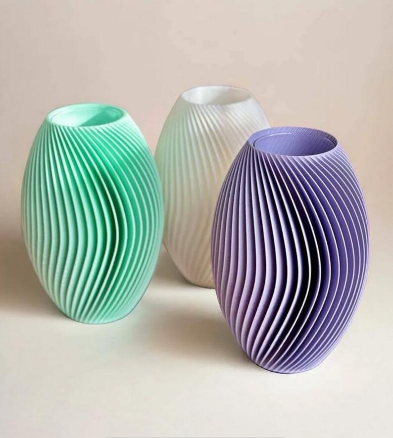 May include: Three decorative vases in shades of green, white, and purple. Each vase has a unique, ribbed design and an oval shape. The vases are arranged on a white surface, creating a modern and minimalist aesthetic.