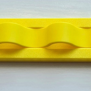 May include: A bright yellow, elongated, rectangular wall-mounted organizer featuring four distinct, wave-shaped loops integrated into the center of the frame. The object has a smooth, matte finish and rounded ends, designed for holding items securely.