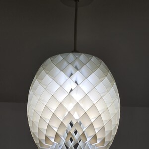May include: White geometric pendant light fixture. The spherical shade is composed of diamond-shaped panels, creating a textured surface. The light hangs from a white rod and ceiling mount, offering a modern design.