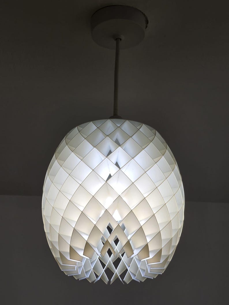 May include: White geometric pendant light fixture. The spherical shade is composed of diamond-shaped panels, creating a textured surface. The light hangs from a white rod and ceiling mount, offering a modern design.