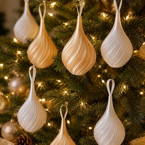 May include: A collection of teardrop-shaped Christmas ornaments featuring a spiraling, ribbed texture. The ornaments are finished in alternating shades of pearlescent white and metallic gold, each suspended by a thin matching ribbon loop.