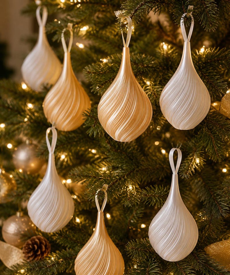 May include: A collection of teardrop-shaped Christmas ornaments featuring a spiraling, ribbed texture. The ornaments are finished in alternating shades of pearlescent white and metallic gold, each suspended by a thin matching ribbon loop.