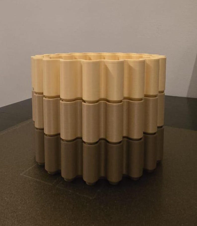 May include: A three-tiered, cylindrical decorative container. The top tier is a light beige color, the middle tier is a medium beige, and the bottom tier is a dark beige. The container has a wavy, repeating pattern around its circumference.