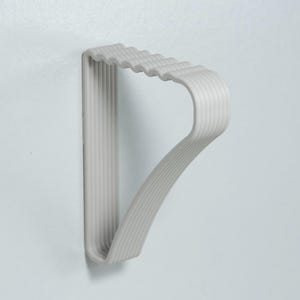 May include: A light gray, wall-mounted coat rack with a unique, curved design. The rack features a series of parallel, vertical lines on the back and a wavy top edge. The curved arm extends outward, creating a functional and stylish storage solution.