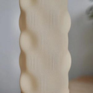 May include: A beige, textured vase with a ribbed design. The vase has a rounded, organic shape with a wooden base. The vertical lines create a visually interesting pattern. The neutral color palette makes it suitable for various decor styles.