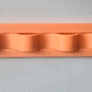 May include: A horizontal, rectangular, peach-colored wall-mounted organizer featuring four rounded, wave-like slots designed for holding items. The object has a smooth, matte finish and a uniform, solid color throughout its entire structure.