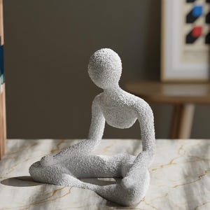May include: A white, textured sculpture of a person in a seated yoga pose. The figure is in a meditative position with legs crossed and arms resting on the knees. The sculpture is on a marble-patterned surface.