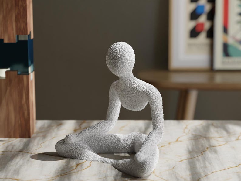 May include: A white, textured sculpture of a person in a seated yoga pose. The figure is in a meditative position with legs crossed and arms resting on the knees. The sculpture is on a marble-patterned surface.