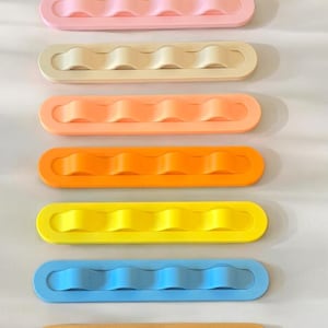 May include: A set of eight rectangular organizers arranged vertically, each featuring a central raised wavy ridge. The colors include green, light pink, cream, peach, orange, yellow, light blue, and tan, all with a smooth, matte finish.