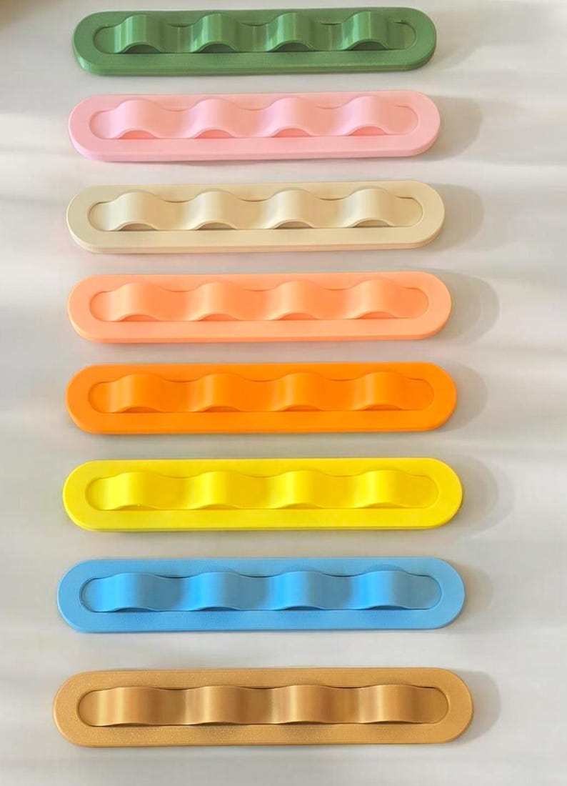 May include: A set of eight rectangular organizers arranged vertically, each featuring a central raised wavy ridge. The colors include green, light pink, cream, peach, orange, yellow, light blue, and tan, all with a smooth, matte finish.